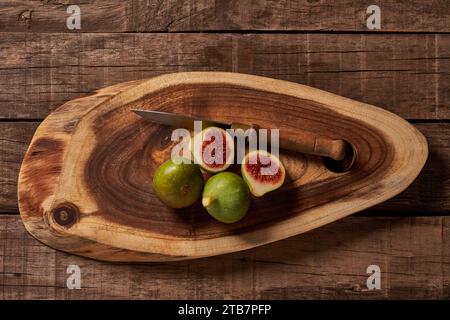 A rustic scene of fresh green figs, one sliced open, on an oval wooden cutting board alongside a vintage knife. Stock Photo