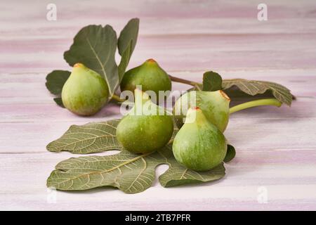 Ripe green figs accompanied by their leaves laid out on a pink wooden surface, conveying a natural and healthy look. Stock Photo