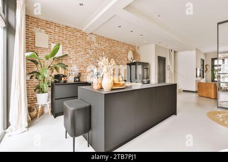 Fruits with decor and utensils on black island in modern kitchen against brick wall at spacious apartment Stock Photo