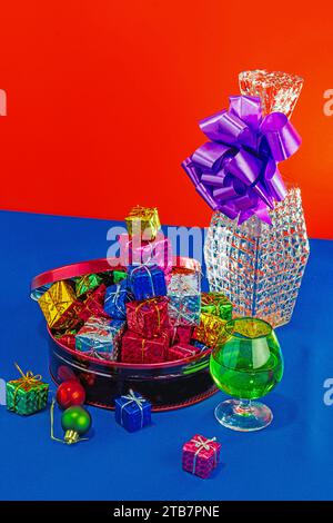Colorful Christmas gifts overflowing from a bowl on a blue table with a large gift in the background against a red and blue backdrop Stock Photo