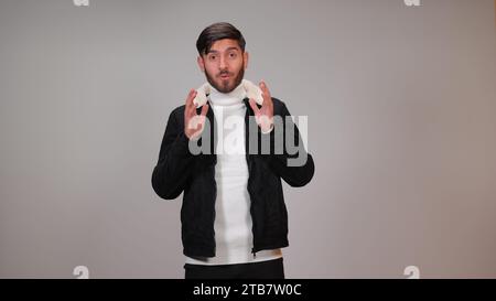 A young man striking a surprised pose against a gray background. Stock Photo