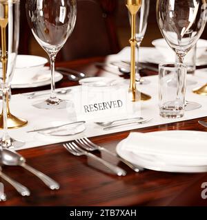 A meticulously arranged dining table with polished cutlery, crystal glassware, and an elegant RESERVED sign indicates an exclusive gastronomic event. Stock Photo