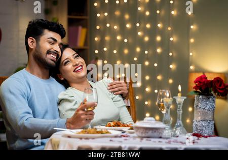 Happy smiling indian couple embracing or hugging during candle light dinner at home - concept of dreaming relationship, romantic and dating. Stock Photo