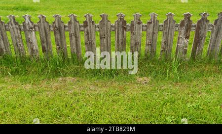 Old wooden picket fence in green grass as rural property boundary Stock Photo
