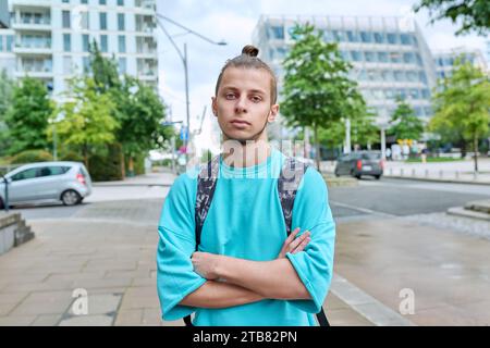 Serious young guy with backpack with crossed arms outdoor, city background Stock Photo