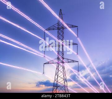 Electric transmission tower with glowing wires against the sunset sky background. High voltage electrical pylon. Energy concept. Stock Photo