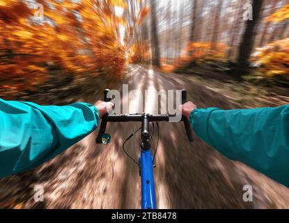 Cyclist rides gravel bike on a trail in the autumn forest. Motion blur effect. First-person view. Stock Photo