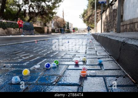 Multi-colored plastic water bottle caps lie on a wet, cobblestone street during the running of the Jerusalem marathon. Stock Photo