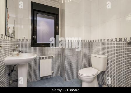 A bathroom with stoneware and white tiles, a dividing border, porcelain sink, matching toilet Stock Photo