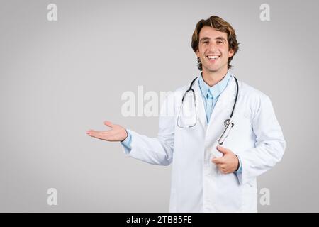 Smiling male doctor in lab coat gesturing with hand on grey background Stock Photo