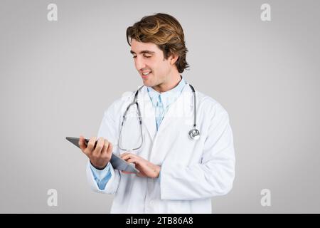 Focused male doctor using digital tablet on grey background Stock Photo