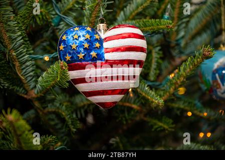 An American flag-shaped heart ornament hangs on a festive Christmas tree Stock Photo