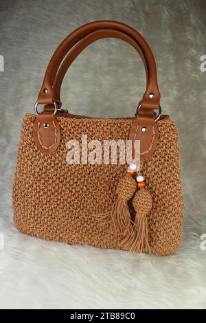 Knitted handmade milky brown bag on furry white blanket. Stock Photo