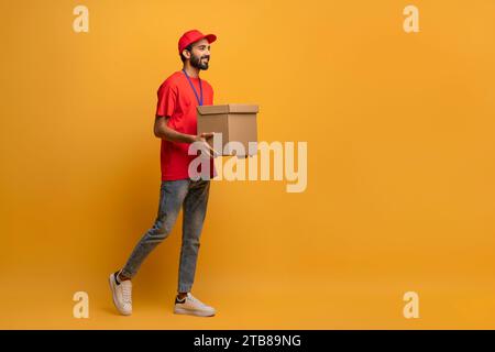 Smiling delivery man in red uniform and cap carrying a cardboard box Stock Photo
