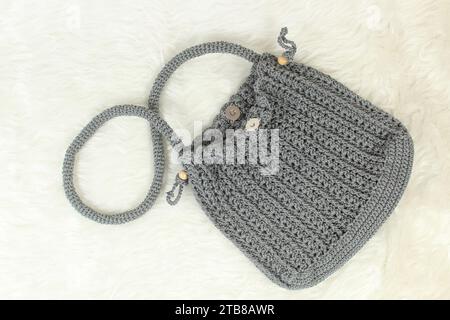 Knitted handmade gray bag on furry white blanket. Top view. Stock Photo