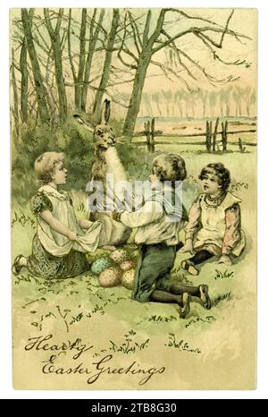 Original charming Edwardian era Easter Greetings postcard. A large magical hare is delivering Easter eggs to beseeching children, a small girl holds out her apron for more eggs. Message is 'hearty Easter greetings'  Postcard dated / posted from Iowa, U.S.A. on 30 March 1907 Stock Photo
