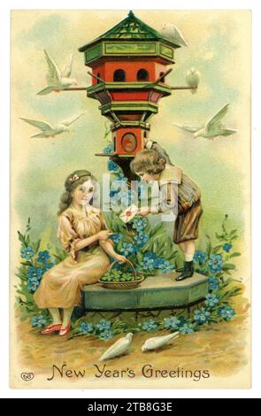 Original Edwardian era embossed American New Year's greeting card,  children next to a dovecote, doves fly around them and the girl has a basket of lucky 4-leaved clover, the boy holds a letter which has been delivered by dove to the dovecote. Circa 1905, U.S.A. Stock Photo
