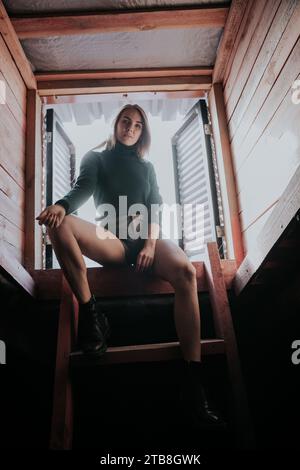 Blonde woman sitting on attic stairs Stock Photo