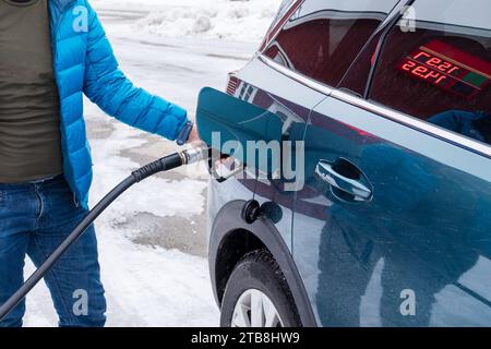 Tourist holding nozzle with refueling oil on modern suv car during the winter travel in Europe at self service gas station Stock Photo