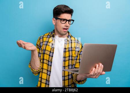 Portrait of clueless guy with stubble wear checkered shirt in glasses look at laptop found bug in code isolated on blue color background Stock Photo
