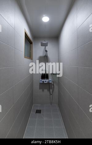 Interior of narrow bathroom with shower water heater and beige ceramic in hostel Stock Photo