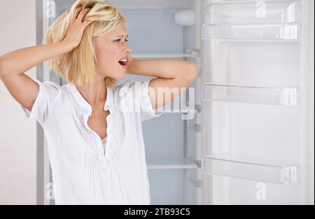 Woman, shocked and empty fridge or hungry stress or poor for meal, upset or frustrated in kitchen. Female person, unhappy concern as worry poverty or Stock Photo