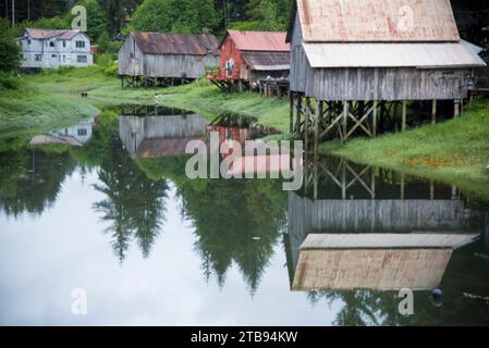 Old wooden boat houses on stilts reflected in water; Petersburg, Alaska, United States of America Stock Photo