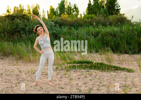 Fit sportive woman exercising outside, warming up before training. Stretching arms and looking away Stock Photo
