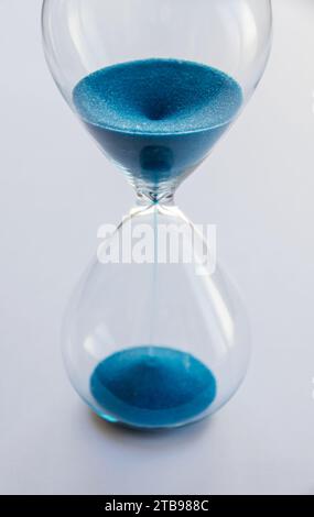 Hourglass containing blue sand isolated on white background. Concept of time passing Stock Photo