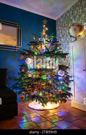 Beautiful christmas tree in a cosy house decorated and lit by light garlands reflecting on the floor. Stock Photo