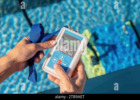 Hands holding a remote control for an automated pool cleaning robot above a swimming pool Stock Photo