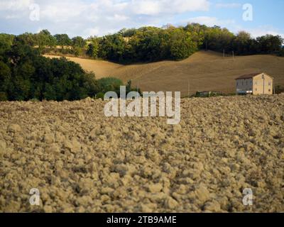 Close-up view of tilled soil with hills, trees and a farmhouse in the background, San Procolo, Monte Vidon Combatte in the Marche Region Stock Photo