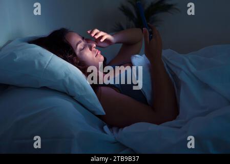 nsomnia and digital addiction: A young lady seeks refuge in her smartphone's glow during the nigh Stock Photo