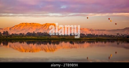 At sunrise, hot air balloons hover above the Nile; Luxor, Egypt Stock Photo