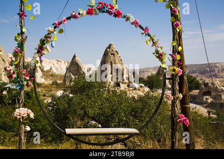 View through a circular swing seat decorated with silk flowers, of the Cave Houses carved into the rock formations against a blue sky near the town... Stock Photo