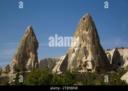 Cave Houses in rock formation peaks against a bright blue sky near the town of Goreme in Pigeon Valley, Cappadocia Region; Nevsehir Province, Turkey Stock Photo