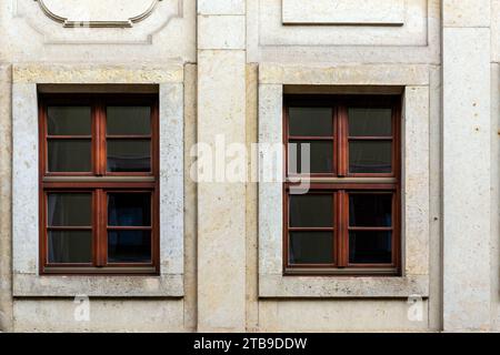 Two rectangular windows with a brown frame on the background of a beige tile wall. From the Windows of the world series. Stock Photo