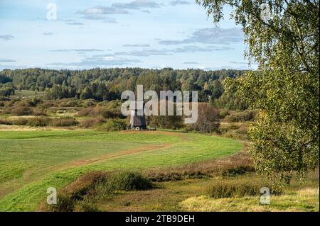 Landscape with a green meadow and a path leading to an old windmill against the background of a forest on a bright sunny autumn day. Stock Photo