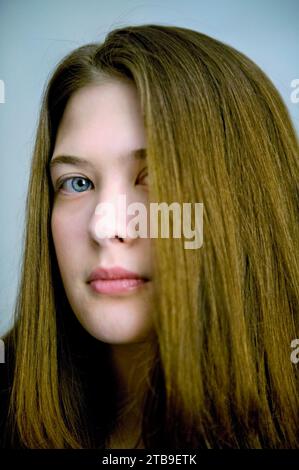 Portrait of a young woman with blue eyes and brunette hair against a blue background; Fairbanks, Alaska, United States of America Stock Photo