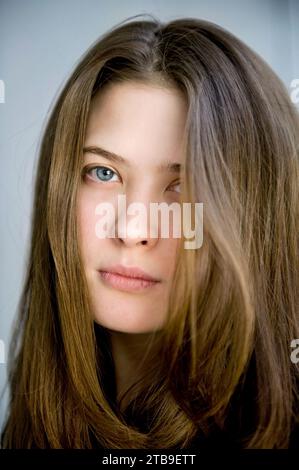 Portrait of a young woman with blue eyes and brunette hair against a blue background; Fairbanks, Alaska, United States of America Stock Photo