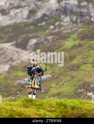 Scottish bagpipe player playing in the hills of the Highlands in Scotland, UK Stock Photo