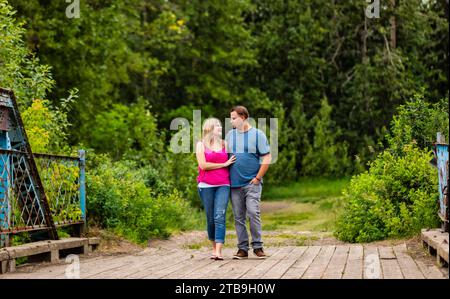 Portrait of a couple walking on a wooden trestle bridge embracing and looking at each other while on a nature walk in a park Stock Photo