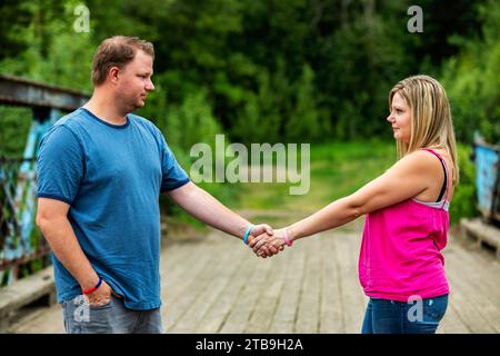 Portrait of a couple standing on a wooden trestle bridge holding hands and looking at each other while on a nature walk in a park Stock Photo