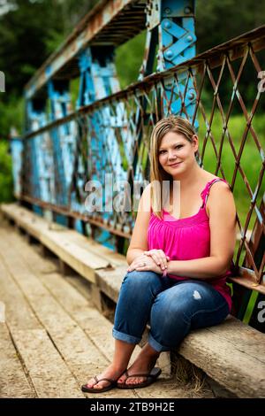 Close-up portrait of a woman sitting on a wooden bench along a trestle bridge during a nature walk in a park, posing for the camera Stock Photo