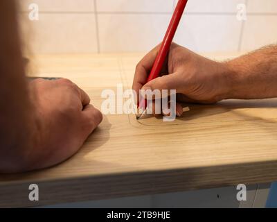 Drawing a line with a pencil on a worktop. The carpenter prepares the wooden part to saw it. Building a new kitchen in an apartment. Working at home. Stock Photo