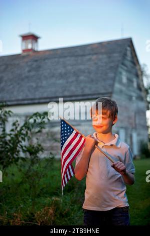 Young, patriotic boy holds up an American flag with an old barn in the background; Lincoln, Nebraska, United States of America Stock Photo