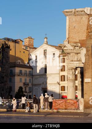 Tourists look at a small white church set within ancient buildings on a autumn evening in the city of Rome, Lazio Region, Italy, December 05, 2023 Stock Photo