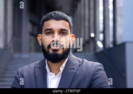Close-up photo of a young serious businessman near an office center in a suit looking confidently into the camera. Stock Photo