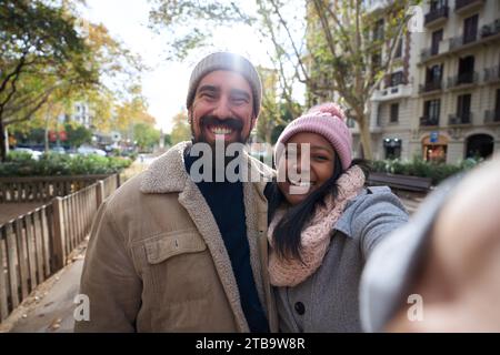 Winter portrait of happy young tourist couple taking selfie outdoors. Smiling multi-ethnic people Stock Photo