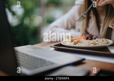 Unrecognizable, female, business employee enjoying her morning meal while working on lap top at modern office. Stock Photo